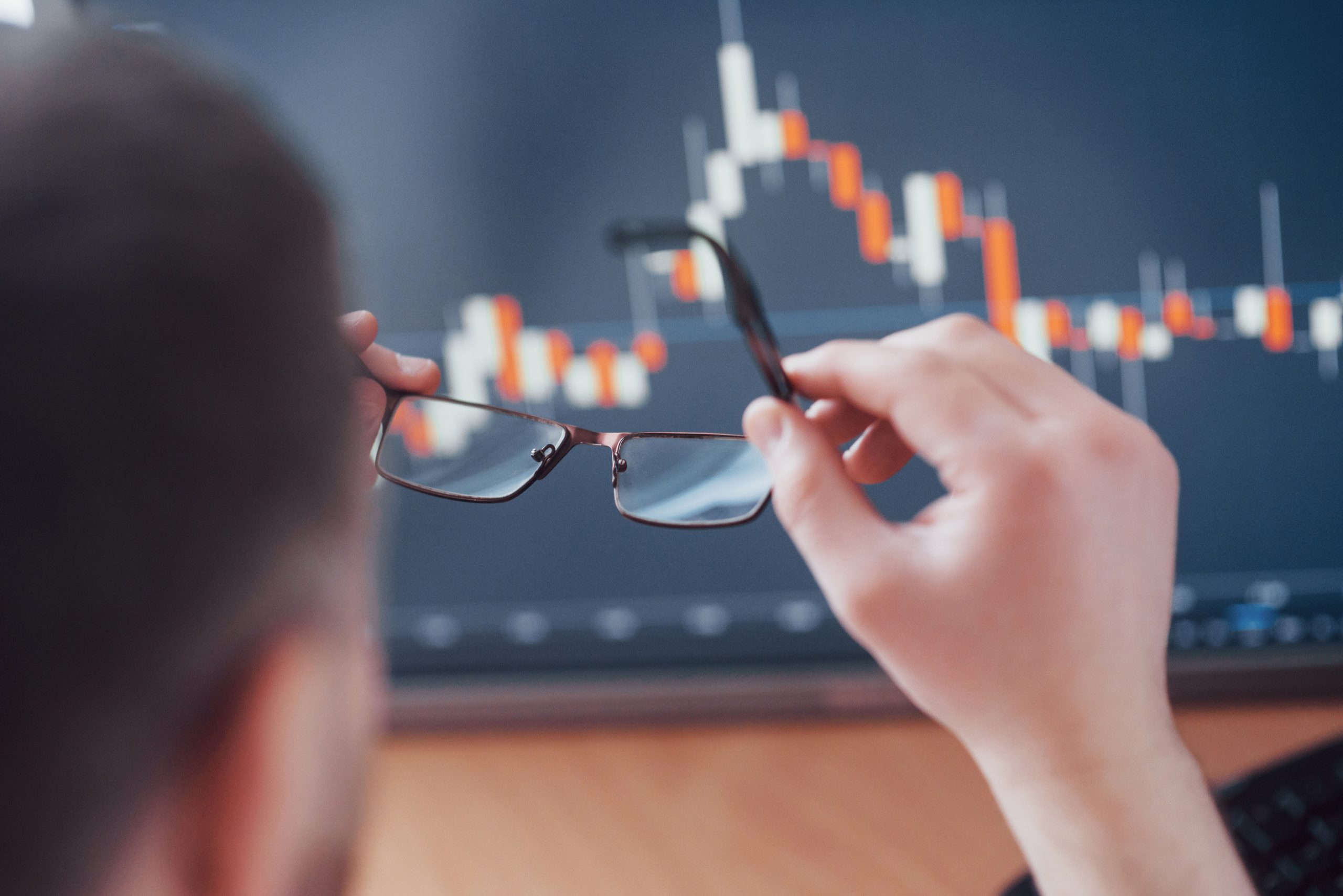 Bom dia Mercado Analyzing data. Close up of a young businessman who holds glasses and looks at the gff while working in a creative office
